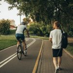 A cyclist and a walker enjoy a peaceful park trail surrounded by greenery.