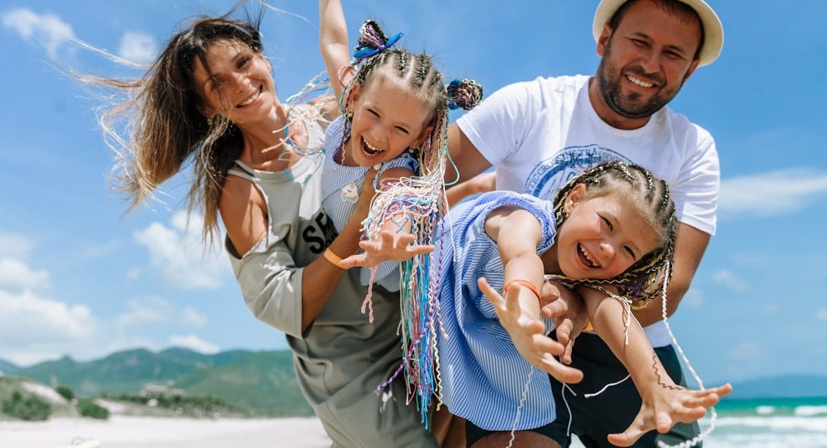 Happy family taking a joyful selfie on a sunny beach vacation, blue sky and summer vibes.