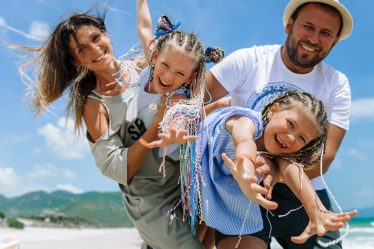 Happy family taking a joyful selfie on a sunny beach vacation, blue sky and summer vibes.